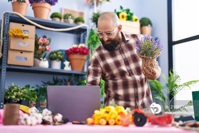 Young bald man florist using laptop holding plant at flower shop