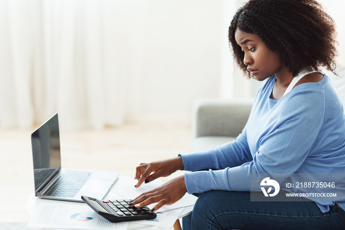 Black woman using calculator and pc at home