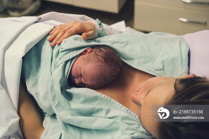 Mother and newborn. Child birth in maternity hospital. Young mom hugging her newborn baby after delivery. Woman giving birth.