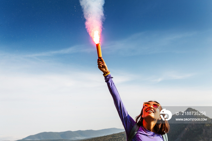 A woman in the wild mountains gives a distress signal SOS using Falsch feuer torch from which comes a bright flame and orange smoke, Concept of emergency situation during hike in the woods