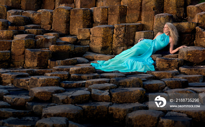 Beautiful blonde woman in turquoise long dress at Giants Causeway in North Ireland