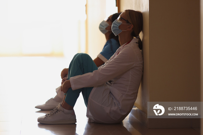 Exhausted nurses after hard long surgery sitting on floor in hall, difficult shift