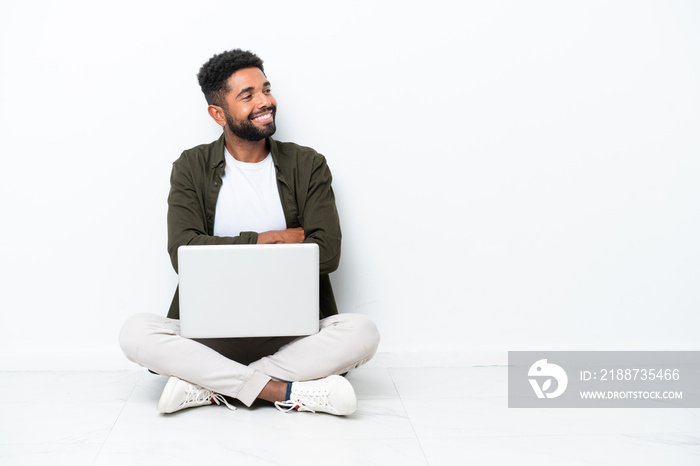 Young Brazilian man with a laptop sitting on the floor isolated on white happy and smiling