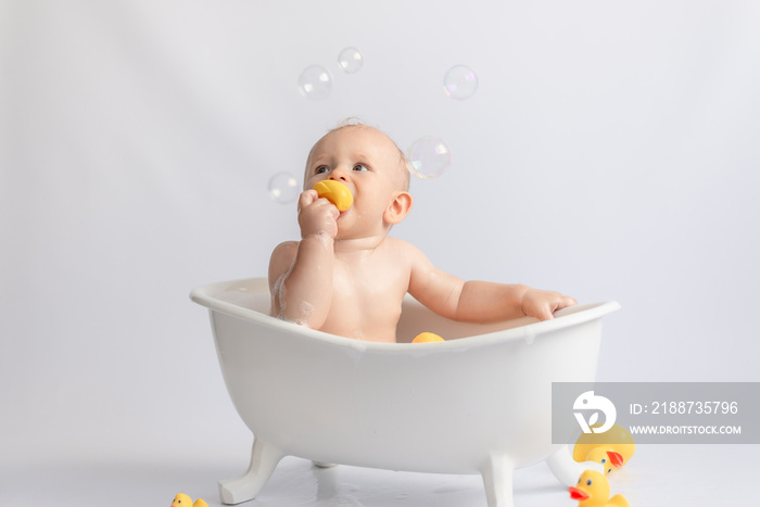 ittle kid likes to swim in a white tub with rubber ducks and foam