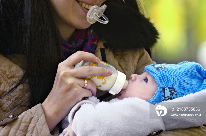 Mother feeding baby son with a bottle in park setting