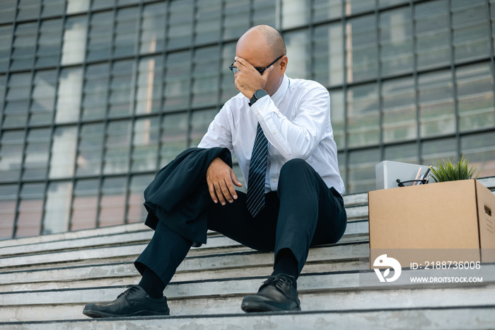 Sadness depressed Businessman with box cardboard packing personal items after losing jobs. Failure businessman sitting at stair front of building. Your fired Unemployed Jobless People Crisis