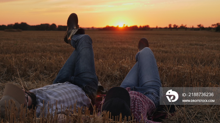 Farmers, man and woman after harvesting, resting lying on straw in wheat field at sunset