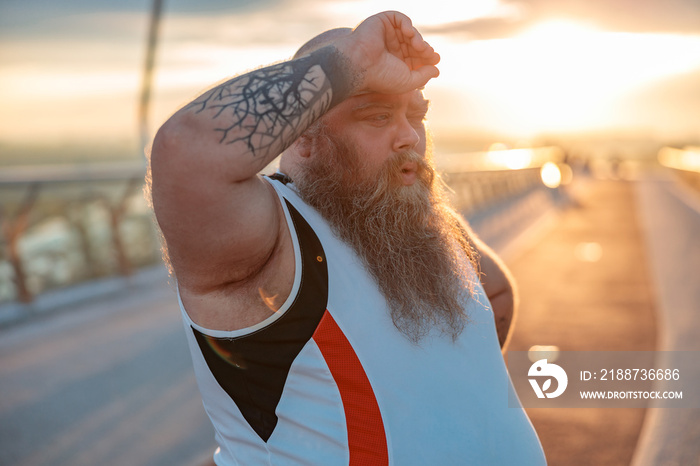 Fat caucasian bearded and bold man with tattoos is doing morning exercses to loose his weight