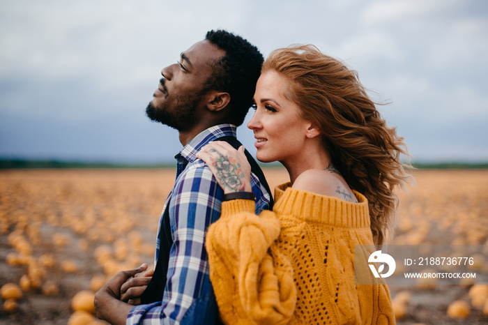 A young woman leaned against her husband’s back while standing in a pumpkin field.