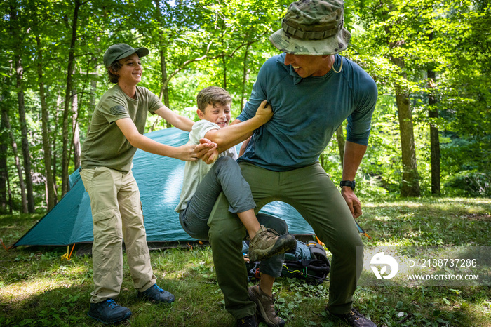 Air Force service member sets up a tent with his sons on  a backpacking trip.