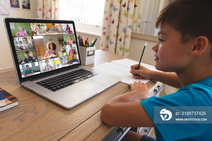 Smiling caucasian boy using laptop for video call, with diverse elementary school pupils on screen