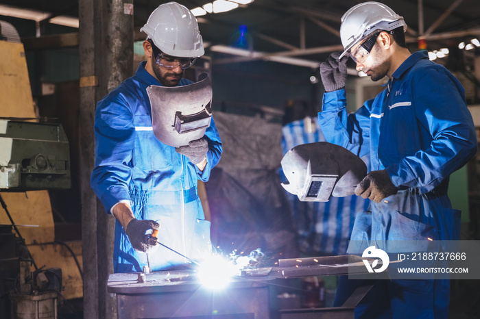 Group of technician industrial engineers wearing safety uniform and safety helmet cutting metal part using hand angle grinder machine. Large industrial factory background.