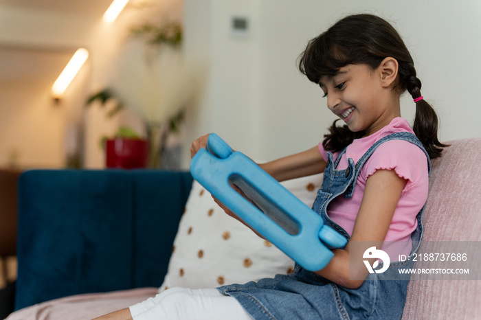 Little girl using tablet while sitting on sofa