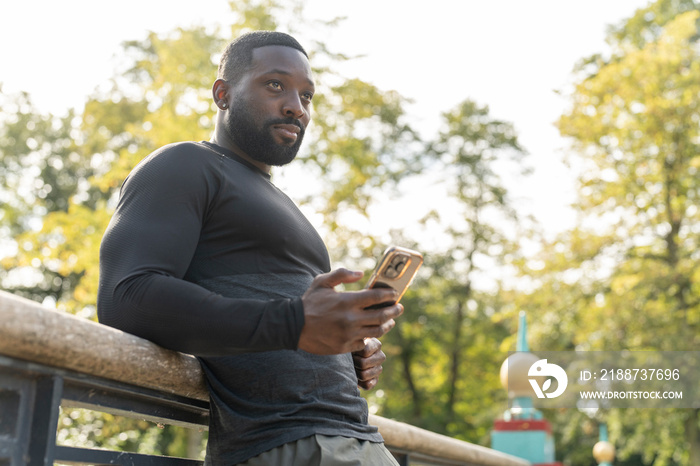 Athletic man with smart phone on footbridge in park