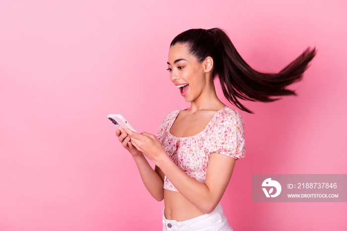 Portrait of astonished funny girl use telephone flying hairdo isolated on pink color background