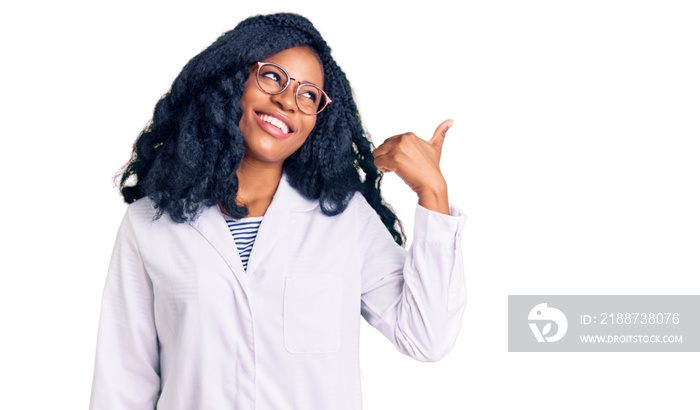 Beautiful african american optician woman with optometry glasses smiling with happy face looking and pointing to the side with thumb up.