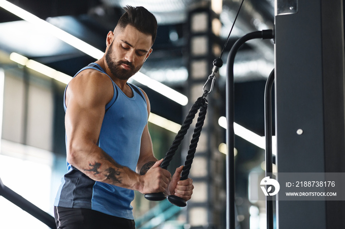 Muscular man exercising with training apparatus in gym