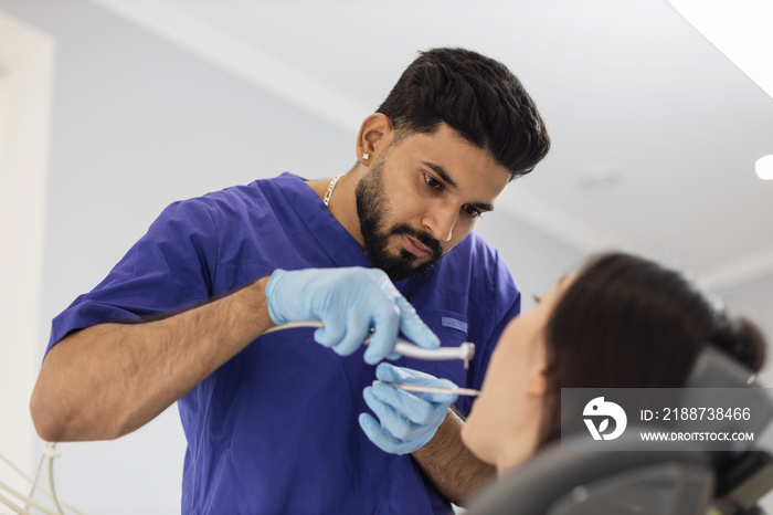 Happy patient and dentist concept. Young bearded asian male stomatologist treating teeth of a beautiful asian woman patient, using tooth drill. Oral health and hygiene.