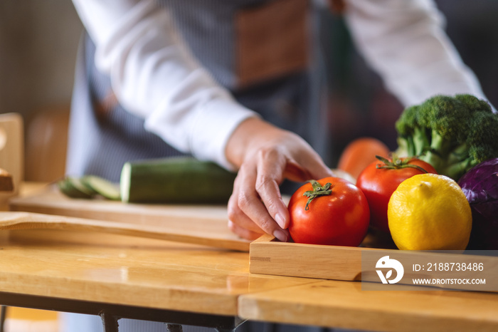 A female chef holding and picking a fresh tomato from a vegetables tray on the table