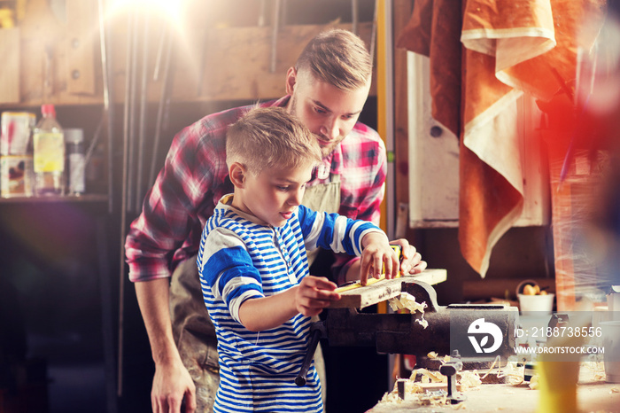 family, carpentry, woodwork and people concept - father and little son with ruler and pencil measuring wood plank at workshop