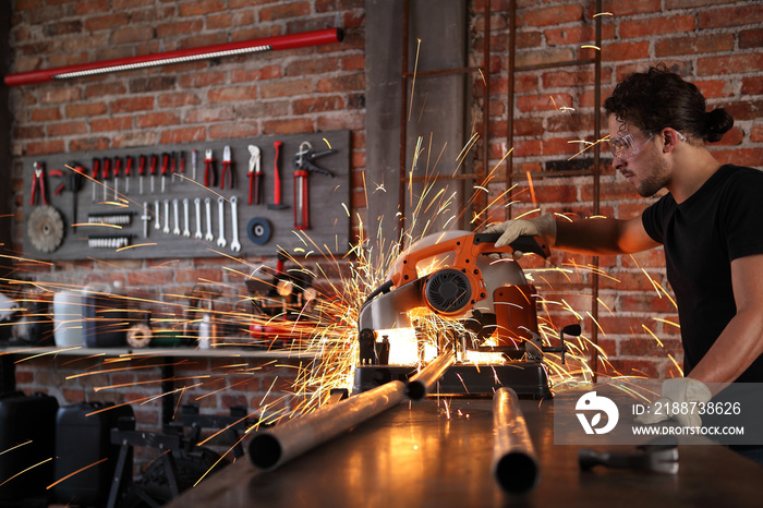 man work in home workshop garage with miter saw, goggles and construction gloves, sawing metal pipe makes sparks, diy and craft concept