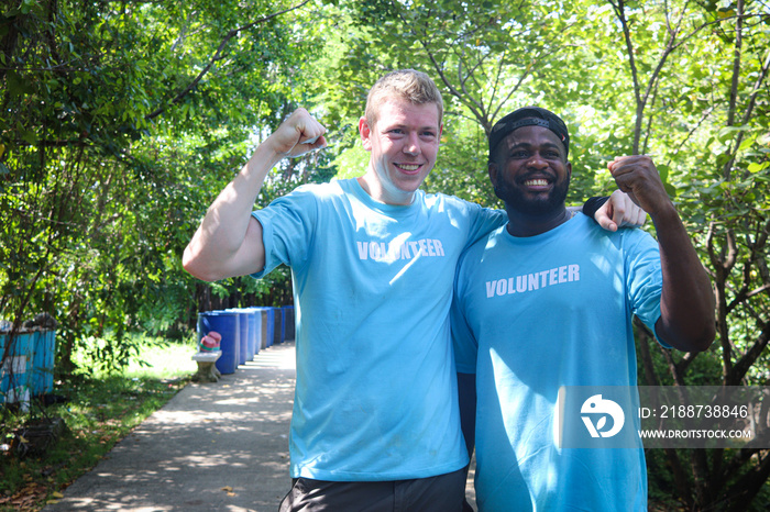 Happy Harmony people do charity work together, smiling Caucasian and African volunteer hug each other and raise fists up, respect in differences race, diversity culture aware of natural environment.