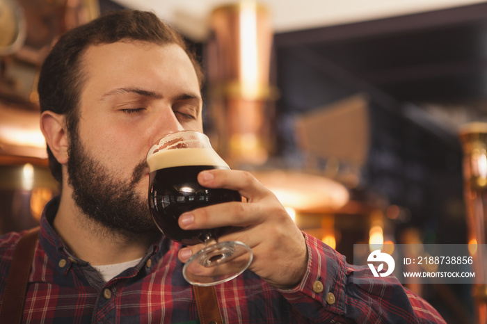 Close up of a brewer sipping delicious beer with his eyes closed, copy space. Professional beermaker enjoying working at his brewery tasting dark beer. Manufacturing, production, sales concept