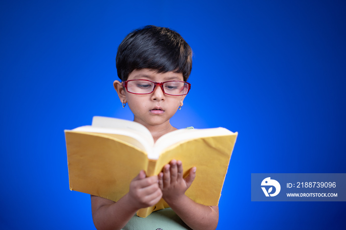 little girl kid with glass and books in hand busy reading from book - concept of book nerd,education and prodigy.