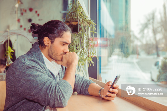 Young man watching smartphone and biting fist in worried expression.