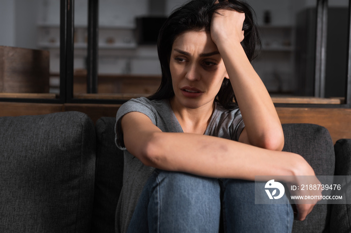 sad woman with bruise on face sitting on sofa, domestic violence concept