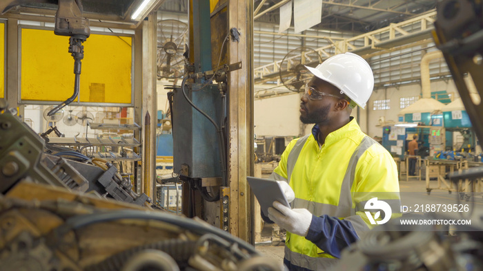 Black African American man, an engineer or worker use tablet device to control smart robot welding hand system automate manufacturing machine engine in factory, industry equipment in operation. People