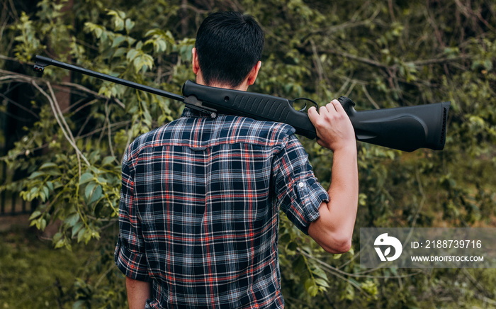 Young man with air rifle on his shoulder. Back view