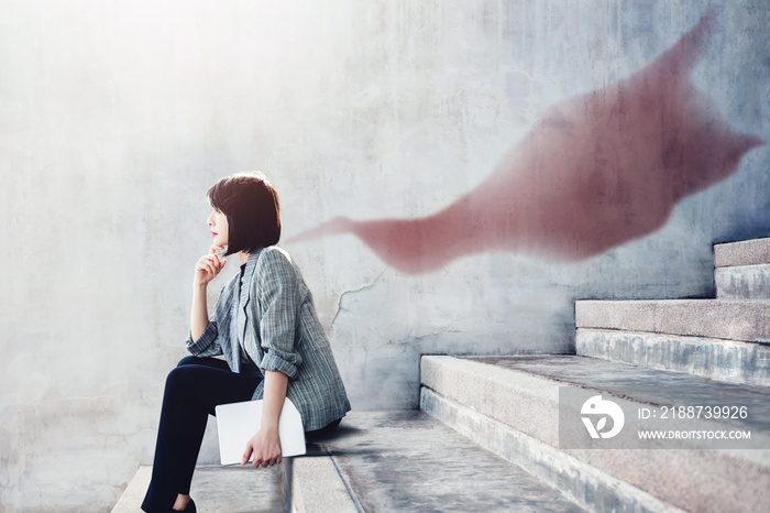 Power, Success and Leadership in Business concept, Working Woman sitting on outdoor Stair and looking Forward with Superhero Blanket Shadow shade on the wall, Side view