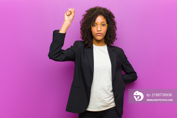 young black business woman feeling serious, strong and rebellious, raising fist up, protesting or fighting for revolution