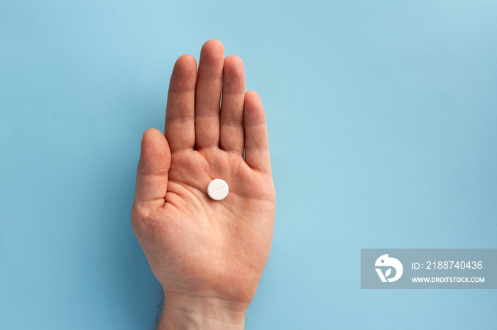 Pill in the male hand, on blue background. Flat lay.