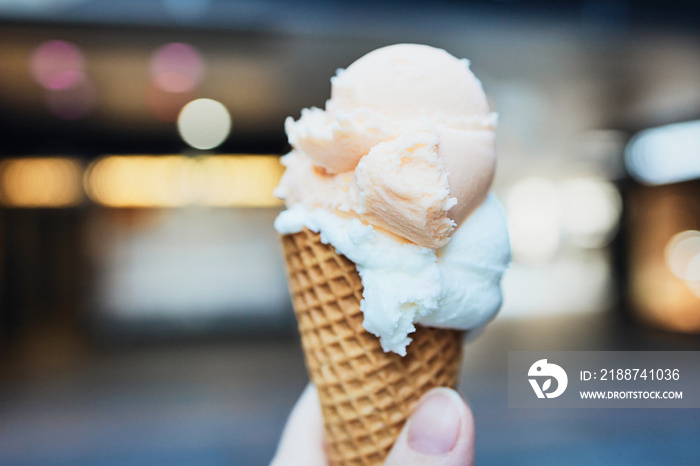 hand is holding ice cream cone in front of shops in a city