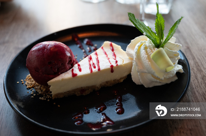 Piece of cheesecake with ricotta served with cassis ice, whipped cream and fresh mint