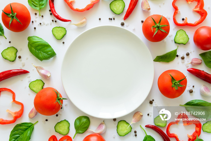 Colorful salad ingredients pattern made of tomatoes, pepper, chili, garlic, cucumber slices, basil and empty plate on white background. Cooking concept. Top view. Flat lay. Copy space