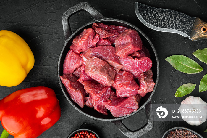 Irish raw Beef Stew Recipe ingredients with sweet bell pepper, in cast iron frying pan, on black stone background, top view flat lay