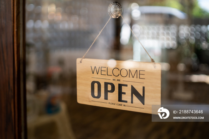 Open sign broad through the door glass bokeh background. OPEN sign board through the glass of store window. text wooden board  door vintage shop sign opened store.