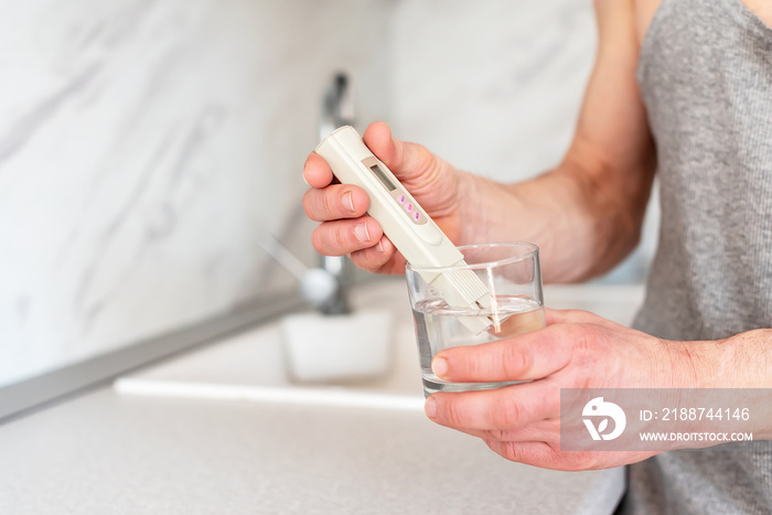 Checking the purity of water at home. Male hands and Glass of water, quality tester and universal litmus ph tester with color scale. Measuring the characteristics of drinking water.