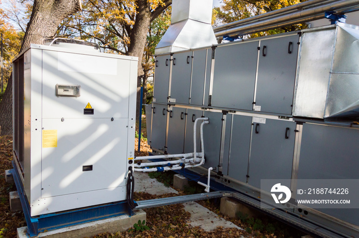 Side view of the gray commercial central air handling unit with cooling coil and big condensing unit standing outdoor on the ground covered by fallen leaves