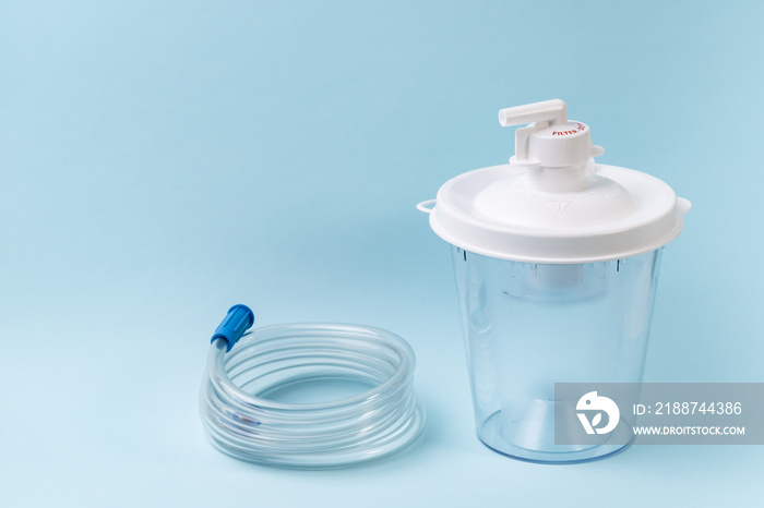 Plastic canister from medical suction machine on blue. Part of portable aspirator used to remove mucus, blood, bodily fluids from patient. Medical equipment using in ambulances and nursing homes