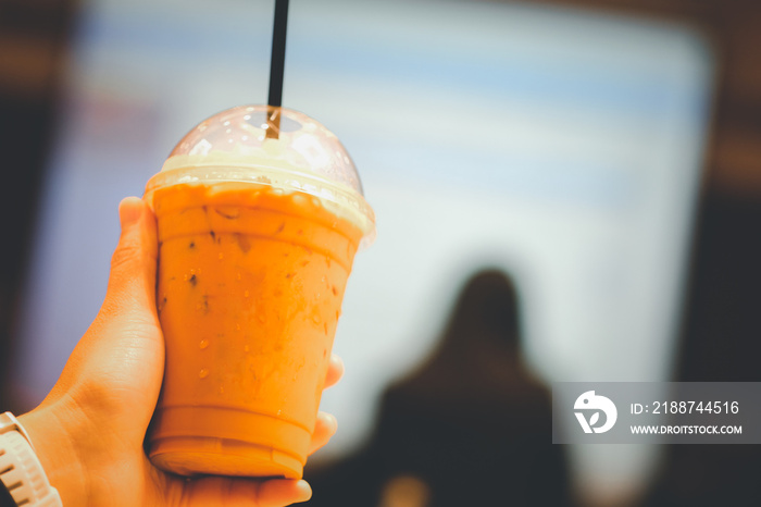 Hand holding a glass of cold Thai milk tea