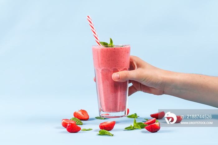 A glass of strawberry smoothie with mint in hand on a blue background