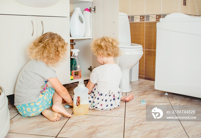 Unattended children play quietly at bathroom with dangerous household chemicals. Safety hazard at home concept. Keep away from children`s reach.