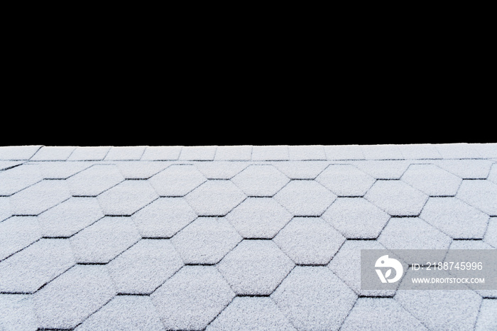 Asphalt roofing shingles texture covered with light snow. House roof shingles covered with frost. Snow covered roof of the house isolated on black background with clipping path.