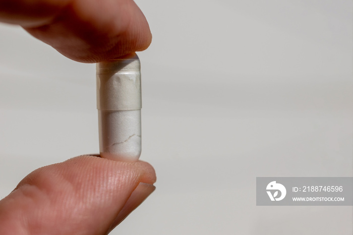 fingers holding manipulated medicine capsule, white background