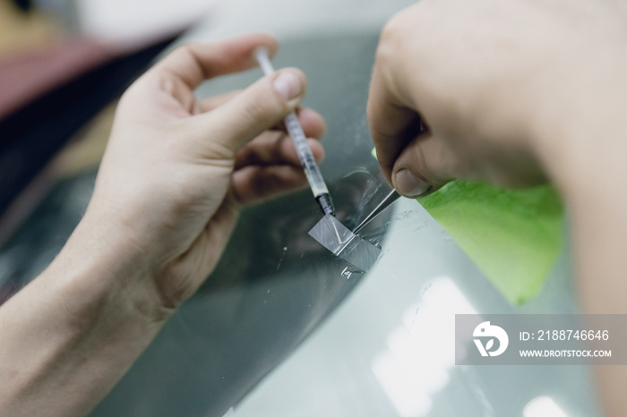 Worker fixes crack in car glass windshield, repair drills and pours epoxy