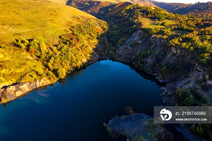 Aerial view of a small lake at sunset, that formed in a former coal mine exploitation, near Resita city, Romania. Captured with a drone, from above, in autumn setting.